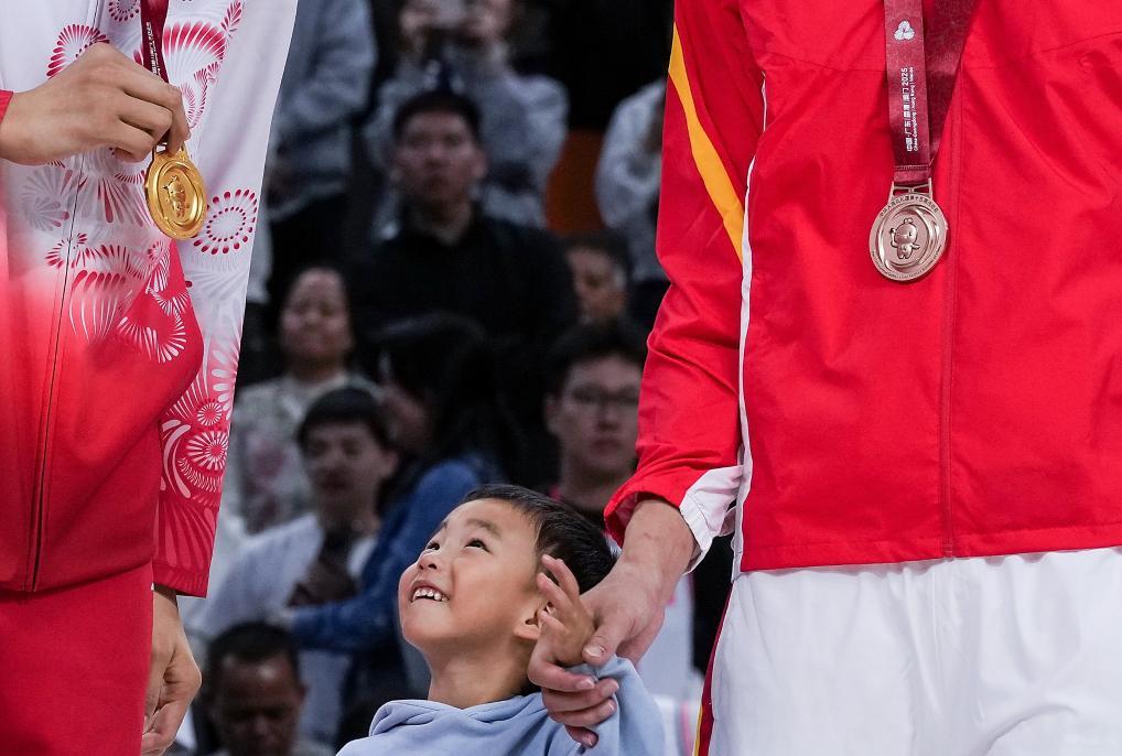 11月12日，在篮球男子成年组决赛中，四川队球员周琦（右）的孩子看着广东队球员沈梓捷（左）的金牌。