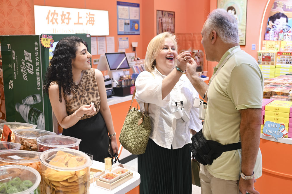2025年7月17日，一名留学生（左）带着父母在位于上海市南京路步行街的一家礼品店内品尝特色食品。在免签“朋友圈”持续扩容以及离境退税“即买即退”政策的推动下，“中国游”持续升温，“中国购”也成为入境游新趋势。作为入境游“第一站”的上海见证了我国强劲的入境游消费活力。